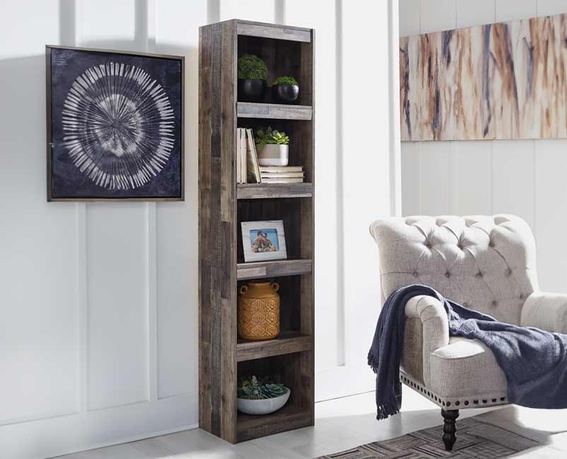 An inviting corner of a room showcasing a tall, rustic wooden bookshelf filled with an assortment of decorative items, including green plants, books, and a woven basket, beside a comfortable tufted armchair with a navy blue throw, under a striking black and white abstract wall art piece, creating a cozy and artistic nook.