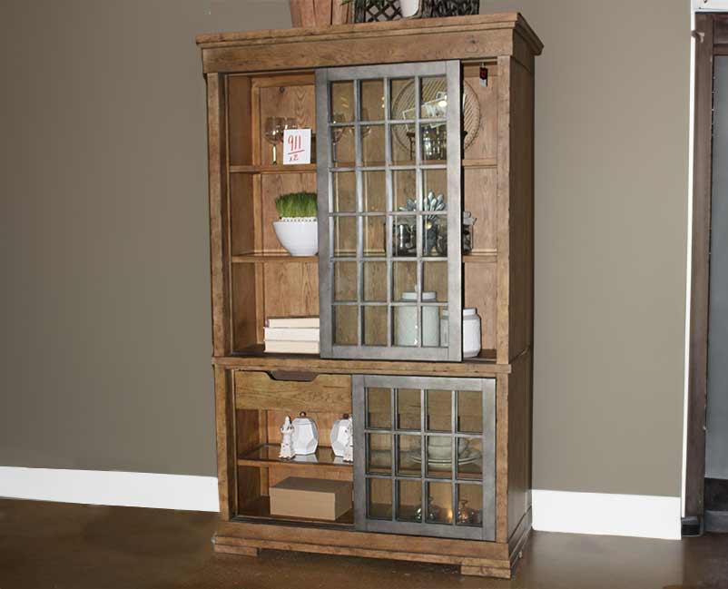Rustic wooden cabinet with glass doors displaying a collection of white pottery, books, and decorative items, set against a neutral wall, creating a warm, homey atmosphere with a vintage touch.